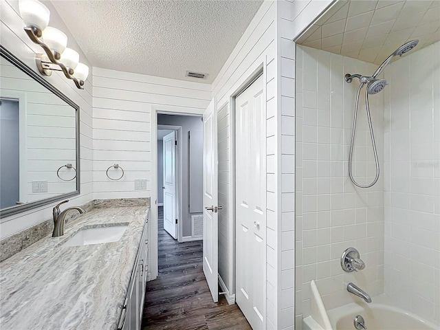 bathroom featuring hardwood / wood-style floors, a textured ceiling, wooden walls, vanity, and tiled shower / bath