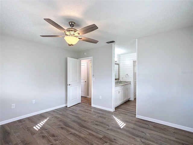 unfurnished bedroom with a textured ceiling, connected bathroom, ceiling fan, and dark wood-type flooring