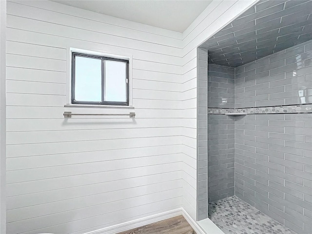 bathroom featuring a tile shower, wood walls, and hardwood / wood-style flooring