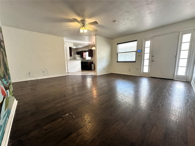 unfurnished living room with dark wood-type flooring, plenty of natural light, and a textured ceiling