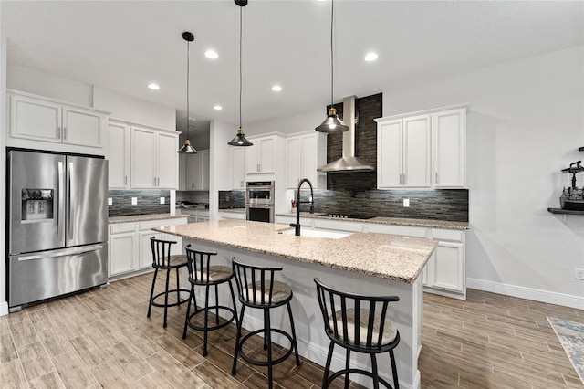 kitchen with white cabinets, appliances with stainless steel finishes, wall chimney exhaust hood, and decorative light fixtures