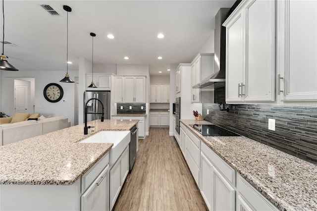 kitchen with light hardwood / wood-style floors, white cabinetry, appliances with stainless steel finishes, decorative light fixtures, and a large island