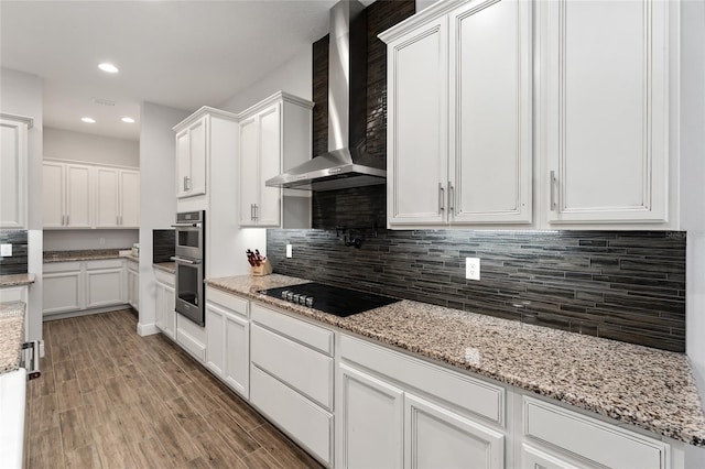 kitchen featuring stainless steel double oven, black electric stovetop, hardwood / wood-style floors, white cabinets, and wall chimney exhaust hood