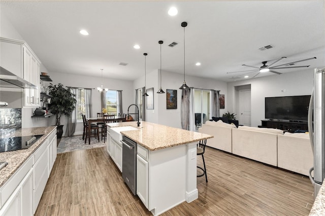 kitchen featuring a center island with sink, white cabinetry, light wood-type flooring, hanging light fixtures, and sink