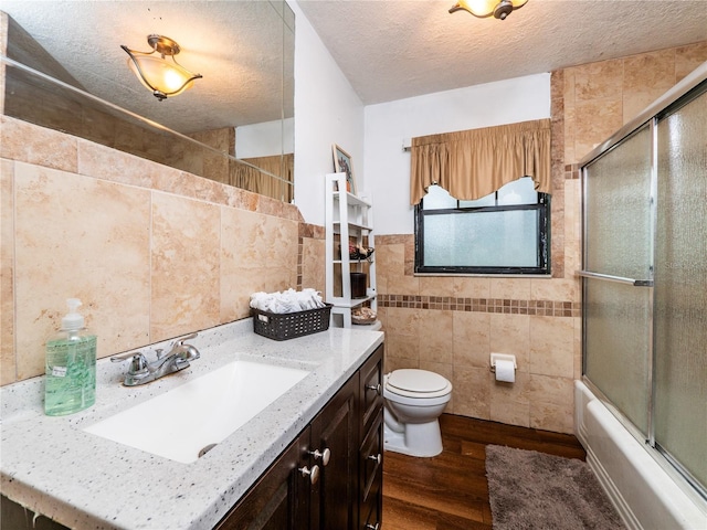 full bathroom featuring toilet, wood-type flooring, tile walls, vanity, and a textured ceiling