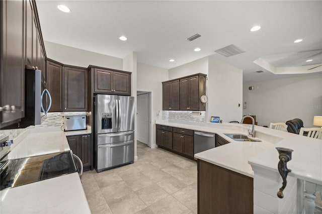 kitchen featuring sink, kitchen peninsula, appliances with stainless steel finishes, dark brown cabinets, and decorative backsplash