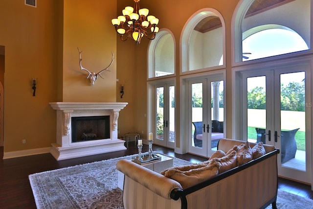 living room with dark hardwood / wood-style flooring, a towering ceiling, an inviting chandelier, and french doors