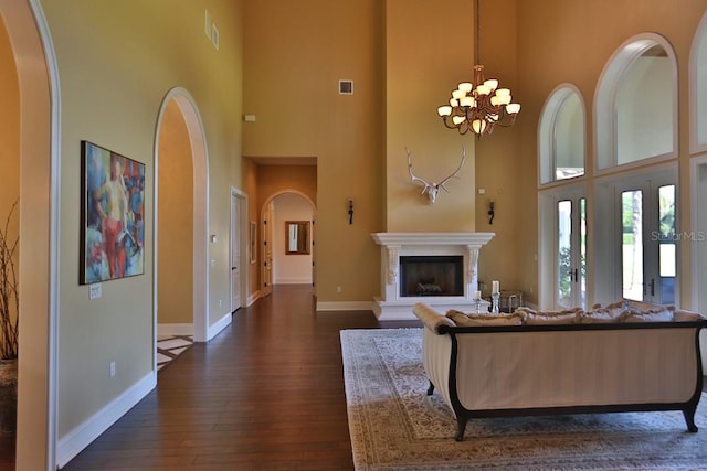 living room with a towering ceiling, dark hardwood / wood-style flooring, and a chandelier