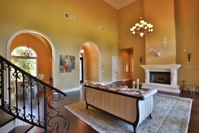 living room featuring dark wood-type flooring, a towering ceiling, a chandelier, and crown molding