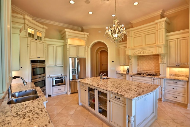 kitchen with decorative light fixtures, light stone counters, sink, and an island with sink