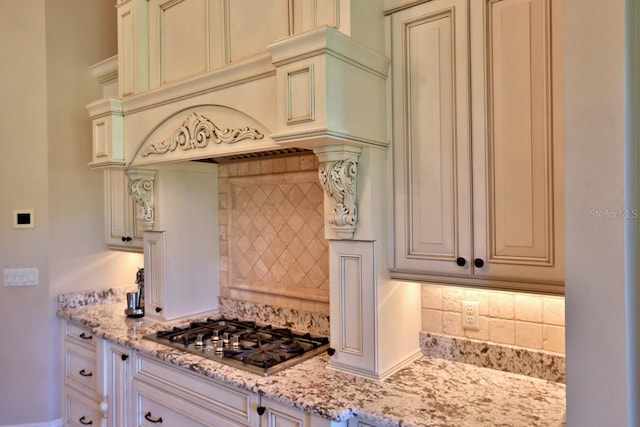 kitchen featuring stainless steel gas cooktop, tasteful backsplash, custom range hood, and light stone countertops