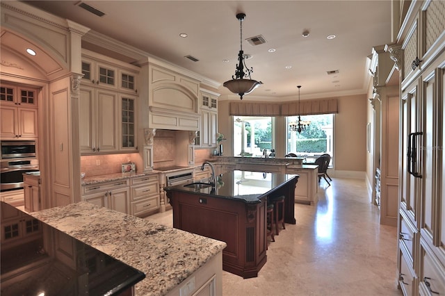 kitchen with pendant lighting, appliances with stainless steel finishes, an island with sink, and cream cabinetry