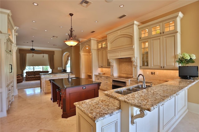 kitchen with cream cabinets, kitchen peninsula, hanging light fixtures, sink, and an island with sink