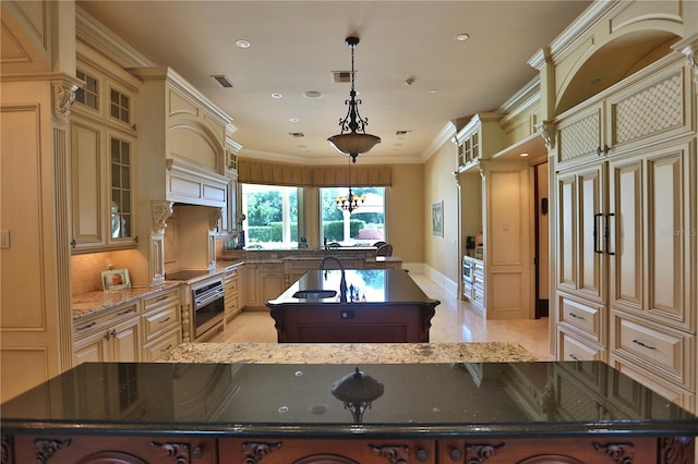 kitchen featuring pendant lighting, cream cabinets, a center island with sink, and dark stone countertops