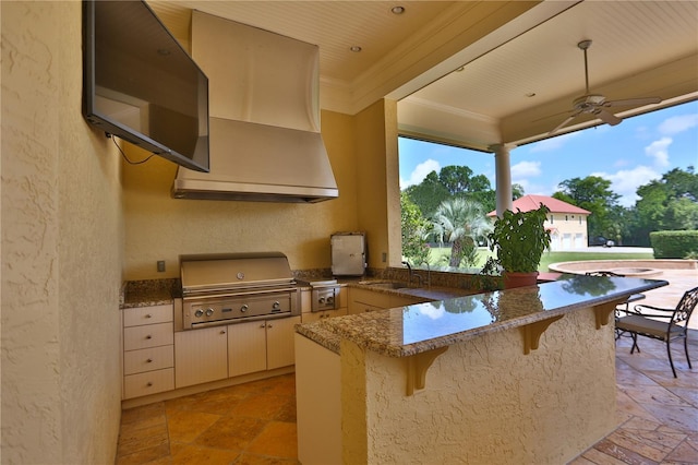 kitchen featuring sink, kitchen peninsula, light stone countertops, a kitchen bar, and range hood