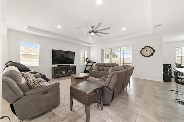 living room featuring ceiling fan, a tray ceiling, and light tile patterned flooring