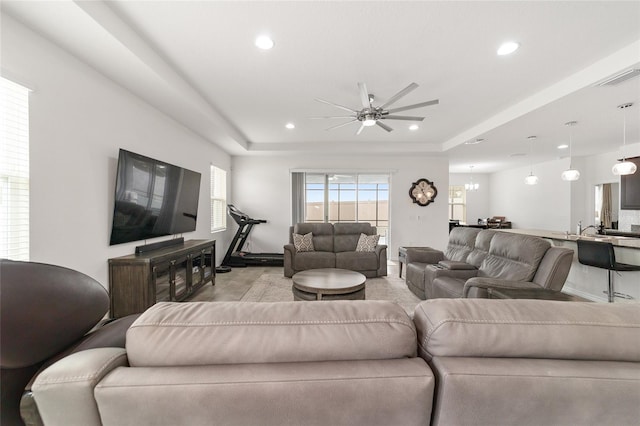 living room with ceiling fan with notable chandelier and a tray ceiling