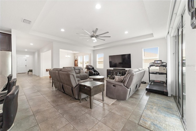 living room with ceiling fan with notable chandelier, a healthy amount of sunlight, and a raised ceiling