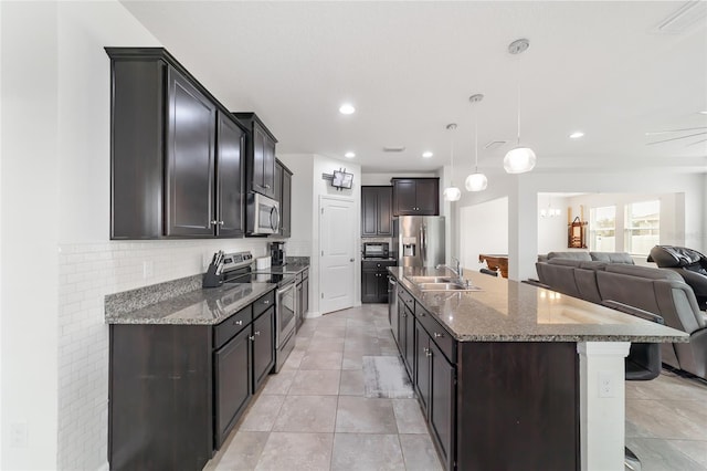 kitchen with appliances with stainless steel finishes, pendant lighting, decorative backsplash, an island with sink, and a breakfast bar