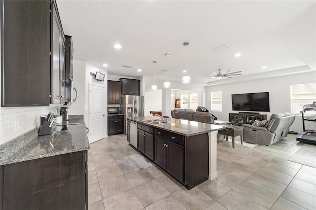 kitchen featuring backsplash, hanging light fixtures, an island with sink, and plenty of natural light