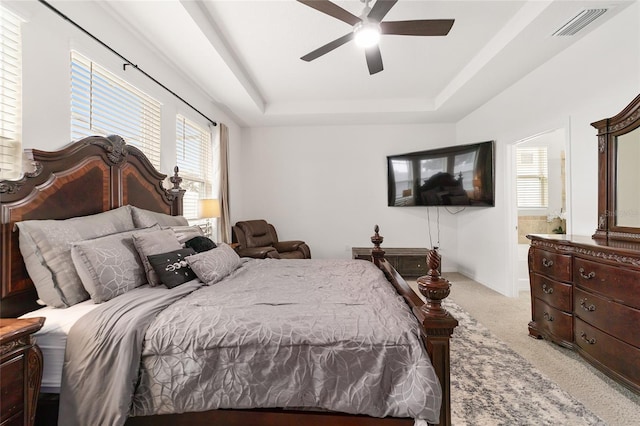 bedroom featuring connected bathroom, light colored carpet, ceiling fan, and a raised ceiling