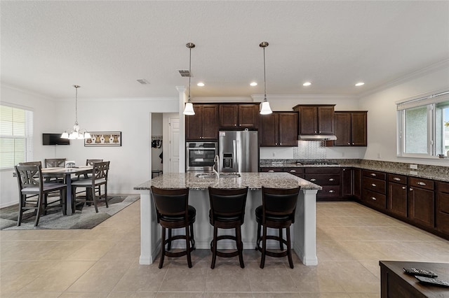 kitchen with sink, an island with sink, stainless steel appliances, dark brown cabinetry, and decorative light fixtures