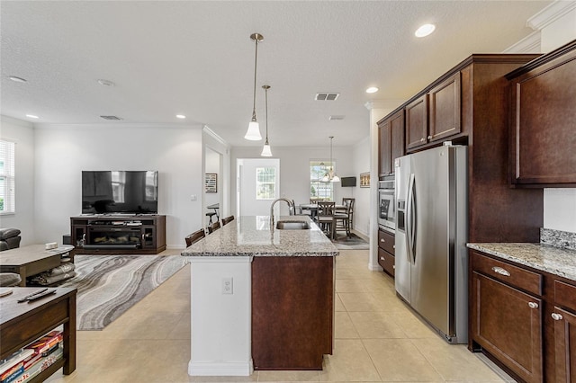 kitchen featuring a center island with sink, pendant lighting, appliances with stainless steel finishes, light stone counters, and a textured ceiling