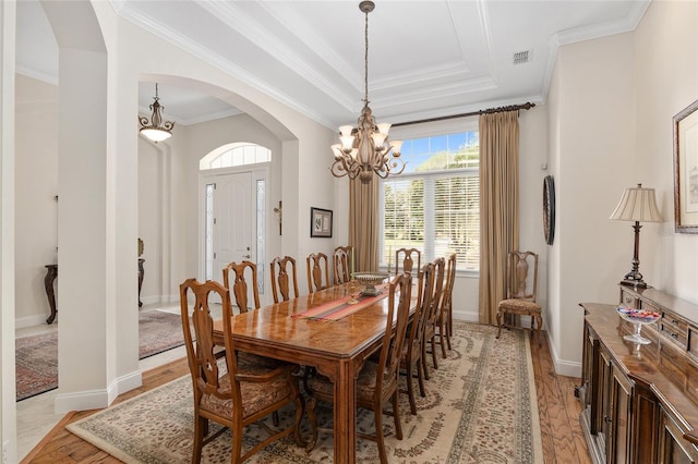 dining space featuring a notable chandelier, light hardwood / wood-style flooring, a raised ceiling, and ornamental molding