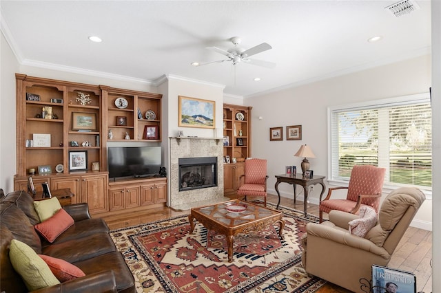 living room featuring ceiling fan, wood-type flooring, a fireplace, and ornamental molding