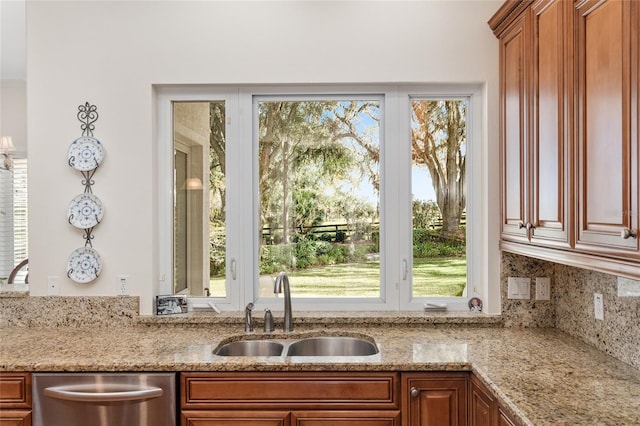 kitchen with stainless steel dishwasher, sink, light stone counters, and plenty of natural light