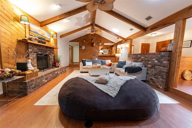 living room featuring a brick fireplace, wood-type flooring, wooden walls, and vaulted ceiling with beams