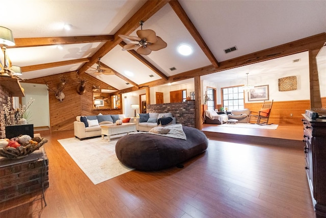 living room featuring lofted ceiling with beams, ceiling fan with notable chandelier, hardwood / wood-style floors, and wooden walls