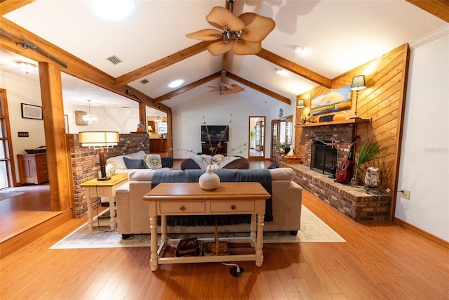 living room with ceiling fan, a brick fireplace, vaulted ceiling with beams, and light hardwood / wood-style flooring