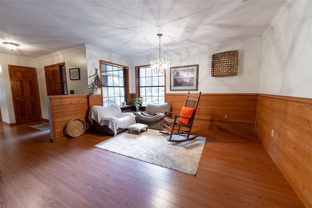 living area featuring wood-type flooring, ornamental molding, a textured ceiling, a notable chandelier, and wood walls