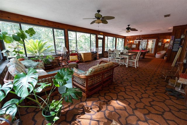 living room with wood walls, a textured ceiling, and ceiling fan