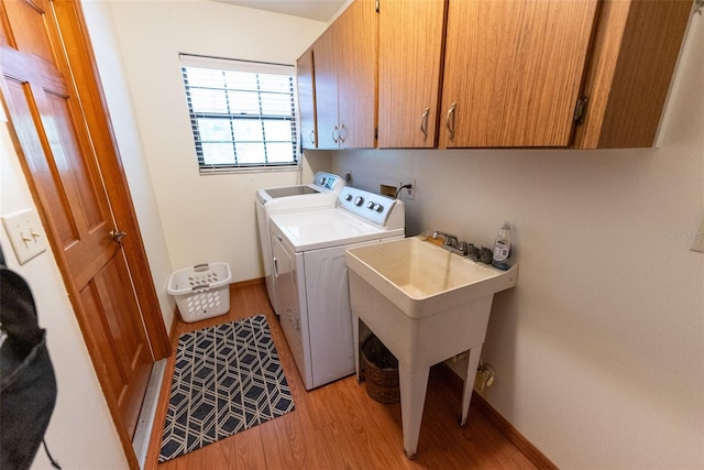 clothes washing area with light hardwood / wood-style flooring, washing machine and dryer, cabinets, and sink