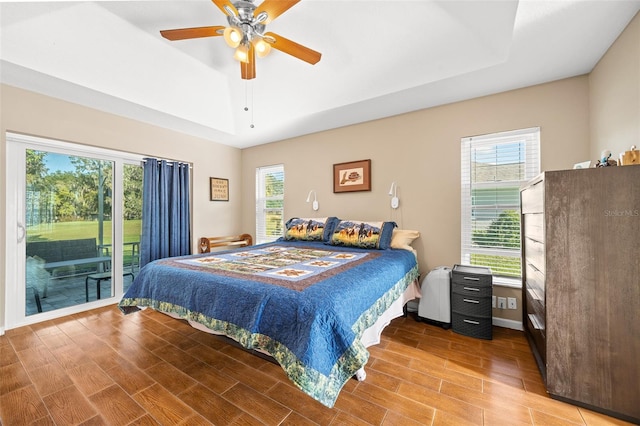 bedroom featuring hardwood / wood-style floors, ceiling fan, a raised ceiling, and access to exterior