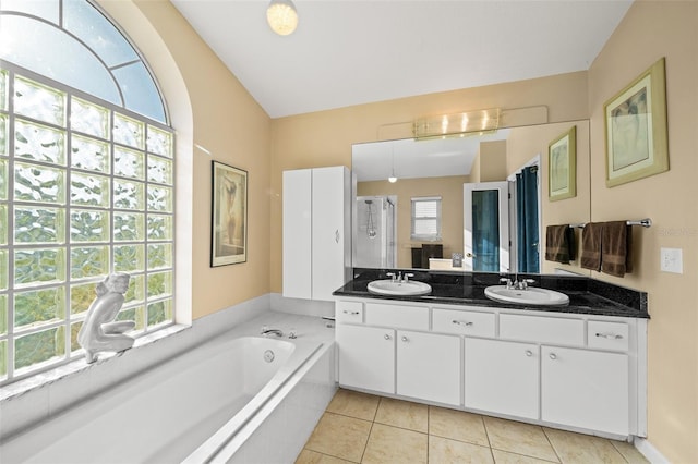 bathroom featuring tile patterned flooring, vanity, a healthy amount of sunlight, and a relaxing tiled tub