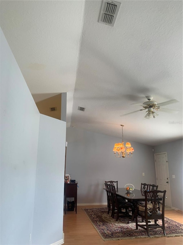 dining space featuring ceiling fan with notable chandelier, wood-type flooring, a textured ceiling, and vaulted ceiling