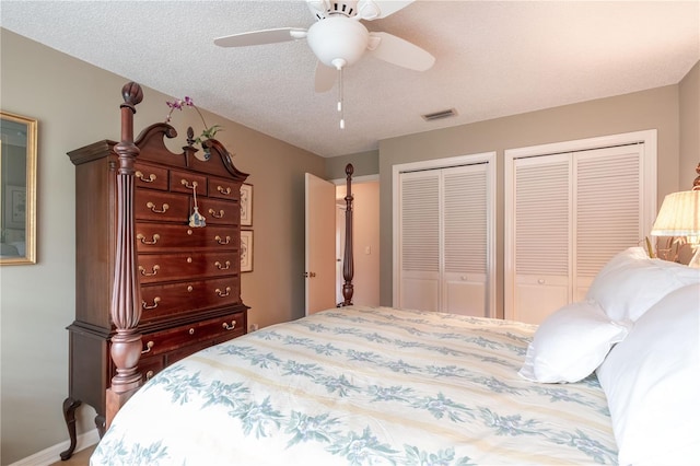 bedroom with a textured ceiling, ceiling fan, and two closets