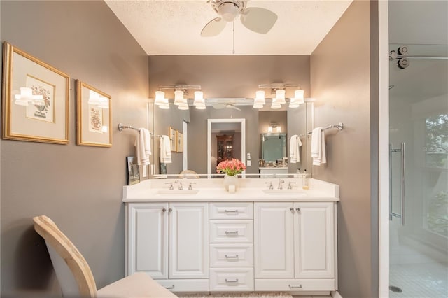 bathroom with ceiling fan, vanity, a shower with shower door, and a textured ceiling