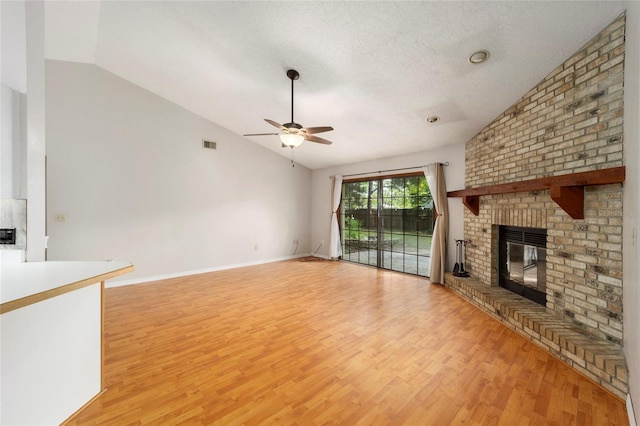 unfurnished living room with light hardwood / wood-style floors, ceiling fan, a textured ceiling, a brick fireplace, and vaulted ceiling