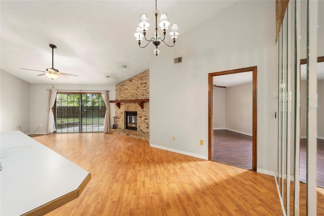 unfurnished living room featuring a brick fireplace, wood-type flooring, high vaulted ceiling, and ceiling fan with notable chandelier