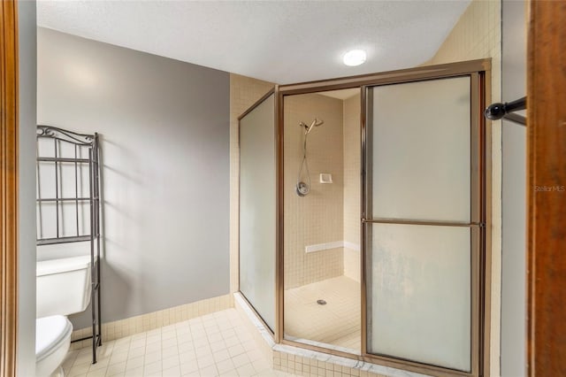 bathroom featuring toilet, a textured ceiling, tile patterned floors, and a shower with door