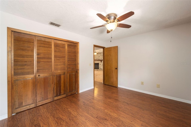 unfurnished bedroom featuring dark hardwood / wood-style flooring, a textured ceiling, ceiling fan, and a fireplace