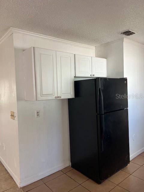 kitchen featuring black fridge, a textured ceiling, ornamental molding, and white cabinets