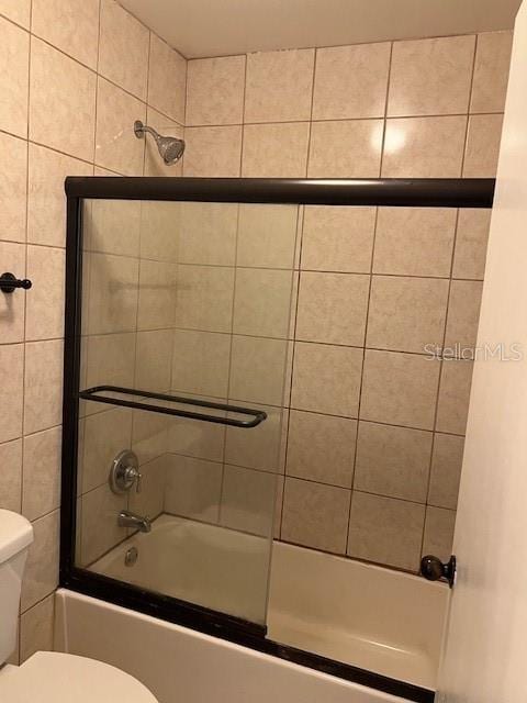 bathroom featuring bath / shower combo with glass door and toilet