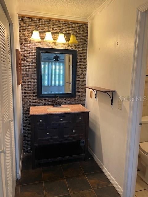 bathroom featuring toilet, a textured ceiling, ornamental molding, vanity, and brick wall