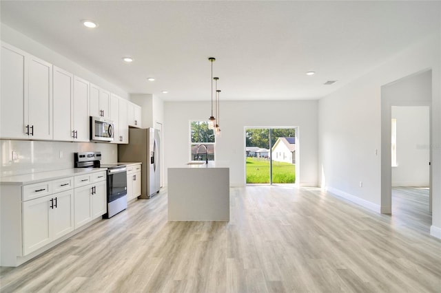 kitchen with white cabinets, stainless steel appliances, hanging light fixtures, and light hardwood / wood-style flooring