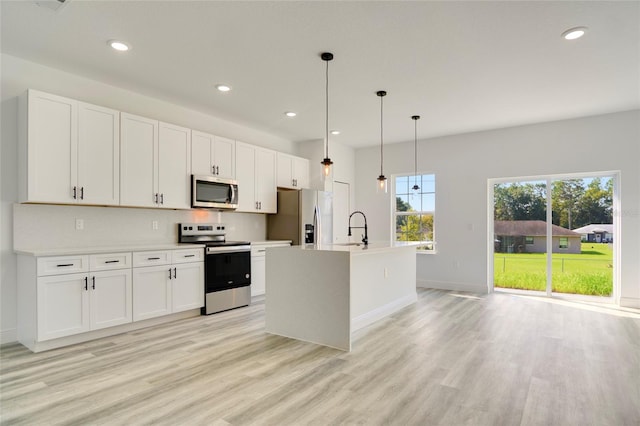 kitchen featuring a kitchen island with sink, stainless steel appliances, white cabinetry, and pendant lighting